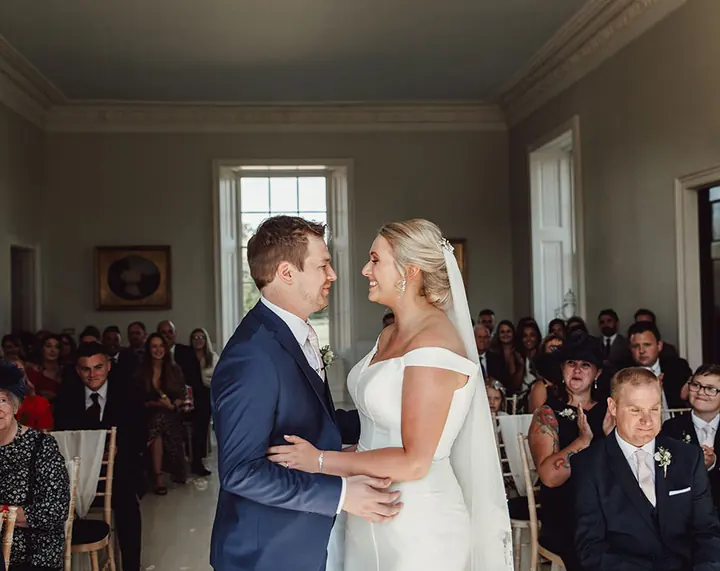 A couple facing each other during the ceremony, guests watching behind them