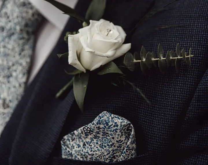 A white rose buttonhole on a navy jacket with a floral pocket square