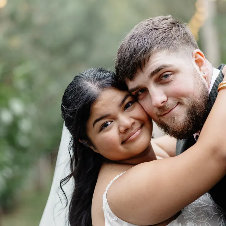 A couple hugging cheek to cheek in a pine-lined walk