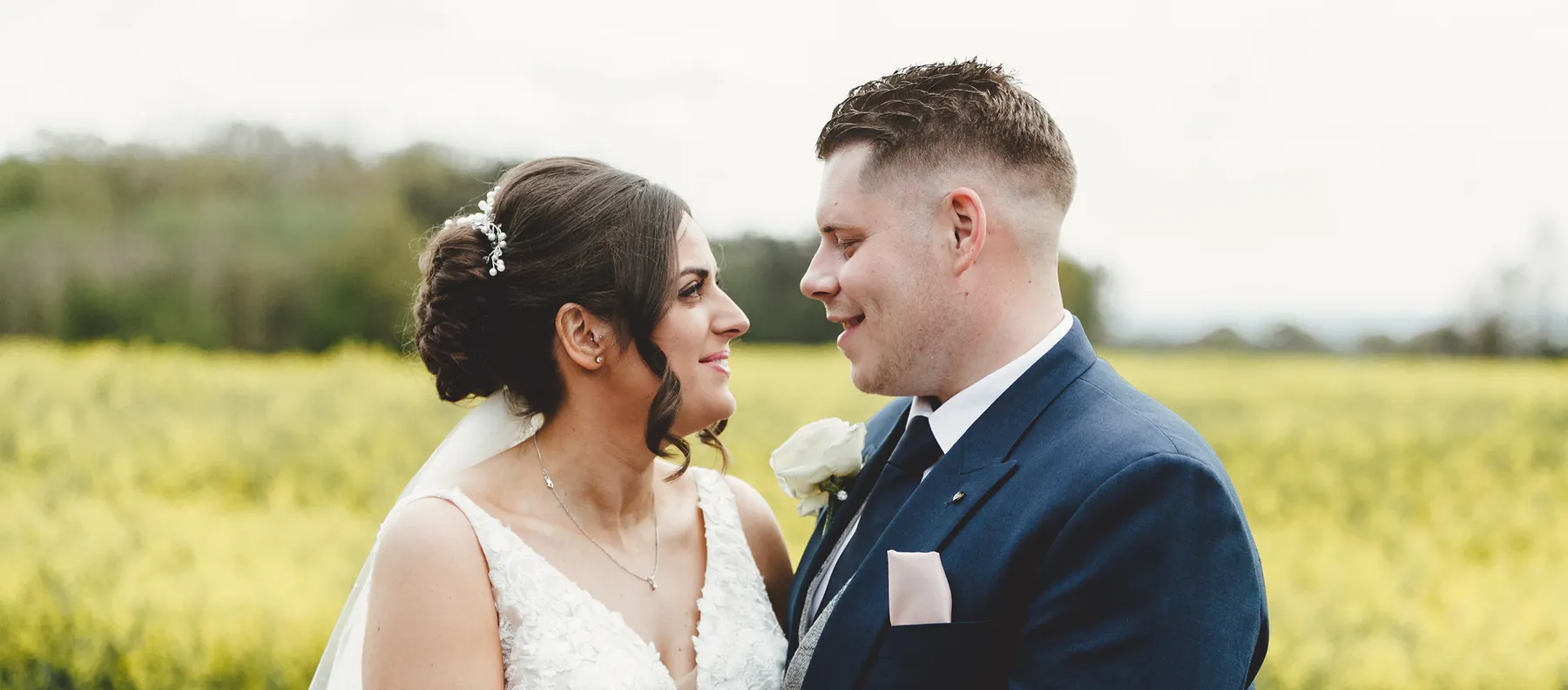 A couple smiling at each other in front of a yellow field