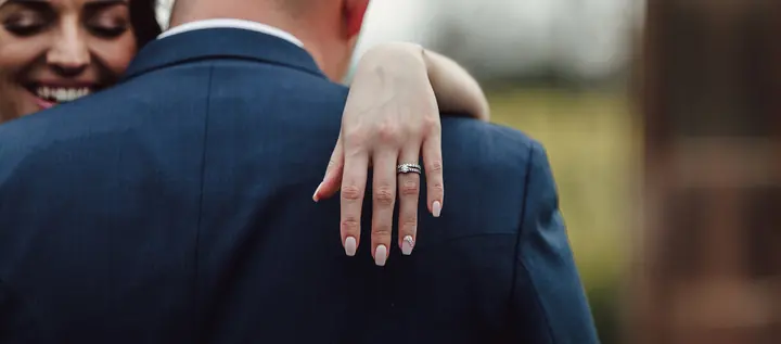 The bride&rsquo;s hand and rings resting on the groom&rsquo;s back