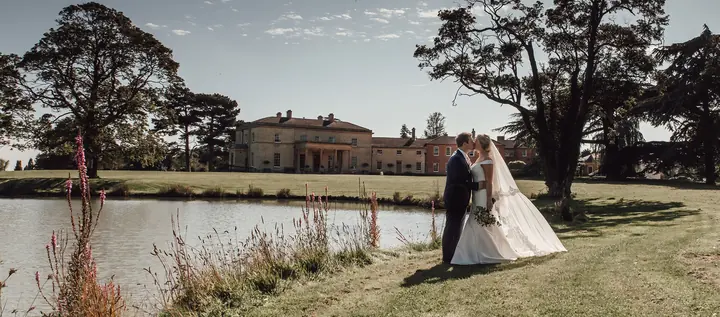 A couple beside the lake with the house behind them