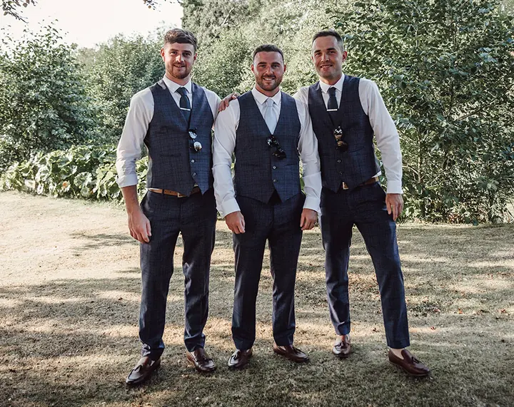 A groom and his groomsmen in waistcoats, standing together in a garden