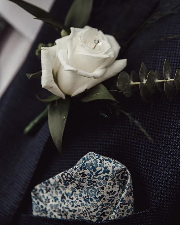 White rose buttonhole and patterned pocket square on a navy suit