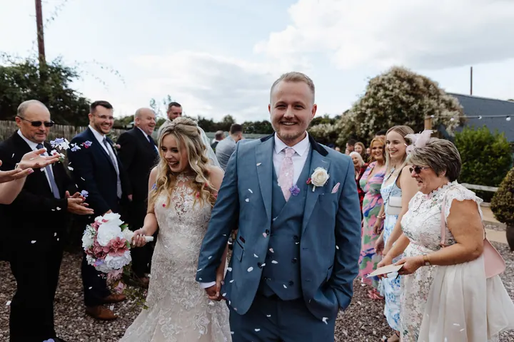 A groom beaming as confetti falls at Coton House Farm