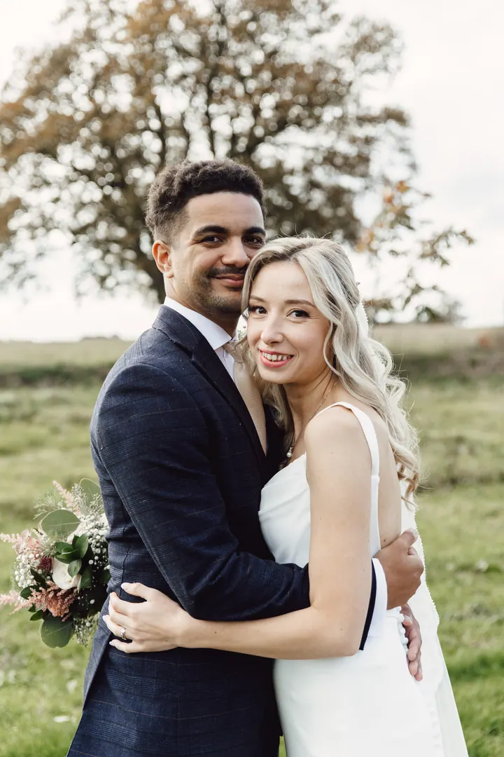 Cicely and Nathan cheek to cheek beneath an autumn oak at Hanbury Wedding Barn
