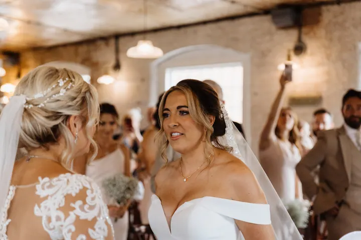 Two brides laughing as they see each other at the front of the ceremony at The West Mill