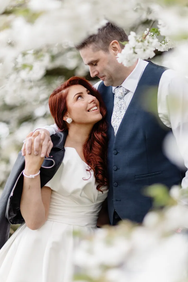 Laura laughing up at Darren beneath white spring blossom at Weston Hall